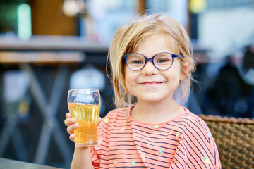 Adorable little girl having breakfast and drinking juice at resort restaurant. Happy preschool...