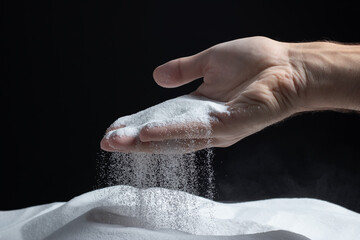 Man with handful of white dry sand in her hands, spilling sand through fingers on black background.