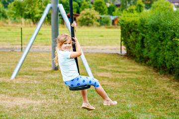 Happy kid girl rids on zip line swing outdoor game play equipment on playground. Child having fun outdoors. Preschool child swinging on summer day. Activity with children.