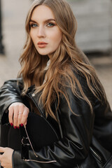 Close up portrait of a beautiful smiling young blonde woman in a black leather jacket on the  a city street background