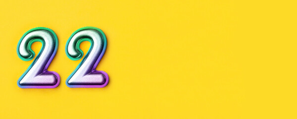 22 years celebration. Banner with birthday greetings. Multi colored metal number twenty two on a yellow background. Copy space, top view.