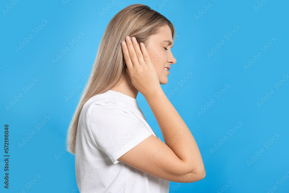 Poster Young woman suffering from ear pain on light blue background