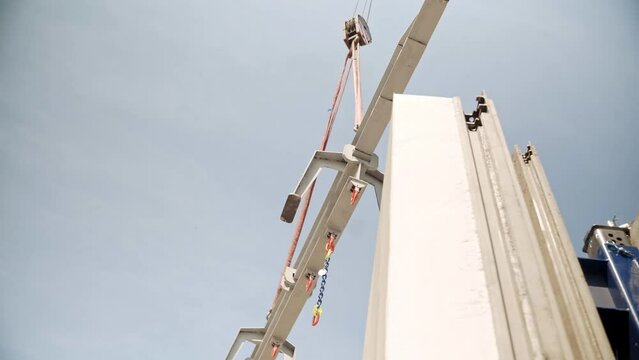 Metal traverse beam hanging secured on crane hook above construction.