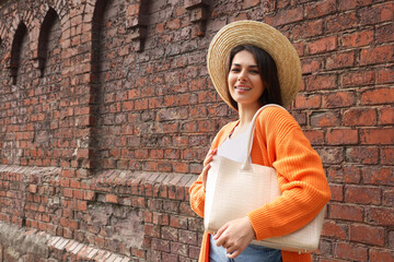 Young woman with stylish bag near red brick wall outdoors, space for text