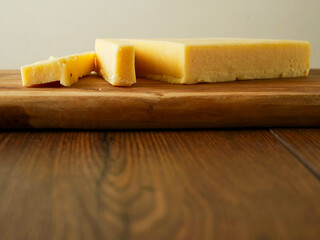 Cut block of red cheddar on a wooden cutting board and table. Premium high quality dairy product...
