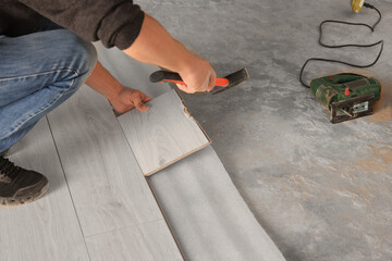 Professional worker using hammer during installation of new laminate flooring, closeup