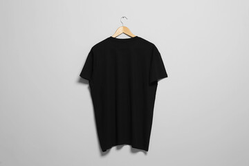 Hanger with black t-shirt on light wall. Mockup for design