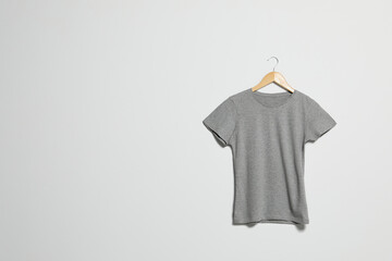 Naklejka premium Hanger with grey t-shirt on light wall. Mockup for design
