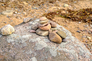 Stack of many small pebbles on top of the big grey round stone laying on pebble beach.
