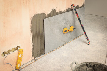 Construction level and yellow suction plate attached to tile on wall indoors