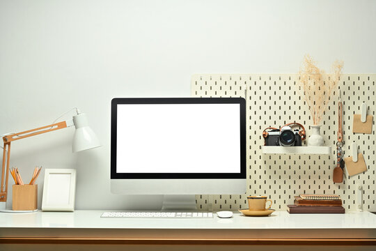 White blank screen computer monitor, picture frame, camera and books on working table. Modern workplace
