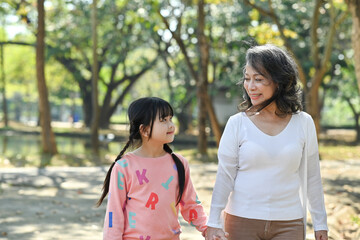 Adorable little child and elderly grandmother walking in the park, spending time outdoor together. Family and love concept