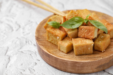 Wooden plate with delicious fried tofu, basil and sesame seeds on light grey table, closeup. Space for text