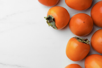 Delicious ripe persimmons on white marble table, flat lay. Space for text