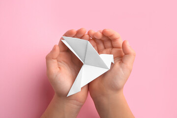 Origami art. Child holding paper bird on pink background, top view