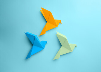 Fototapeta na wymiar Origami art. Colorful handmade paper birds on light blue background, flat lay