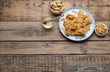 Delicious peanut kozinaki bars, nuts and honey on wooden table, flat lay. Space for text