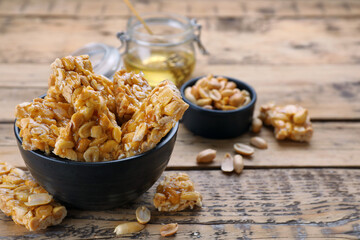 Delicious peanut kozinaki bars in bowl on wooden table, space for text