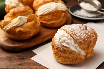 Delicious profiteroles with cream filling and powdered sugar on wooden table, closeup