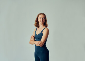 Young caucasian woman in sportswear looking over shoulder with arms crossed in studio