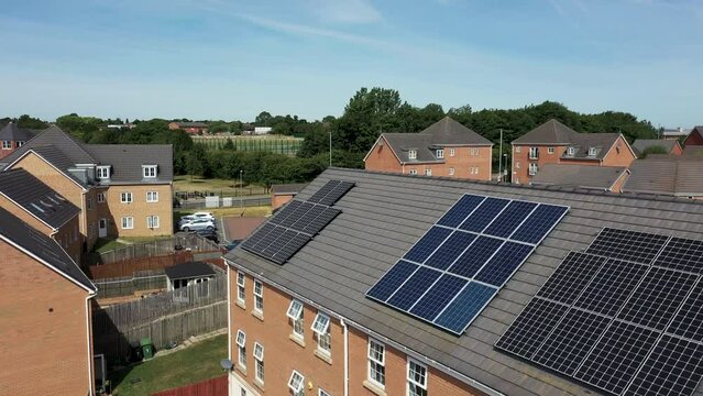 Aerial drone footage of a British house with solar panels on the roof, on a sunny summers day.