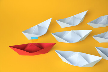 Group of paper boats following red one on yellow background. Leadership concept