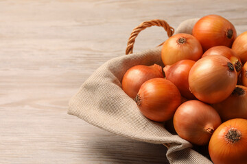 Wicker basket with many ripe onions on wooden table, closeup. Space for text