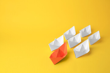 Group of paper boats following orange one on yellow background, space for text. Leadership concept