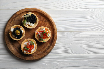 Delicious tartlets with red and black caviar served on white wooden table, top view. Space for text