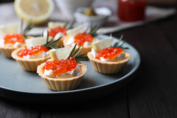 Delicious tartlets with red caviar and cream cheese served on wooden table, closeup