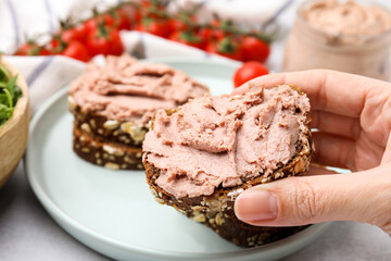 Woman holding delicious liverwurst sandwich at white table, closeup