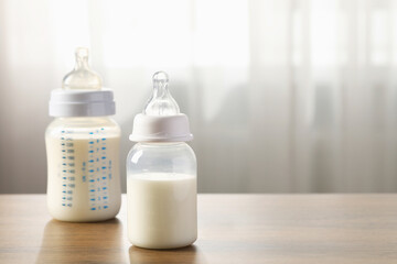 Feeding bottles with milk on wooden table indoors. Space for text