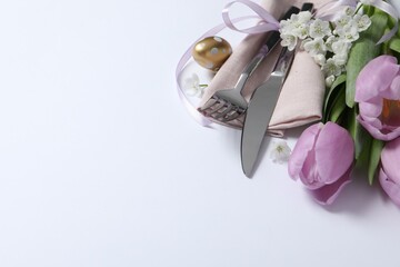 Cutlery set, Easter egg and beautiful flowers on white background, space for text. Festive table setting