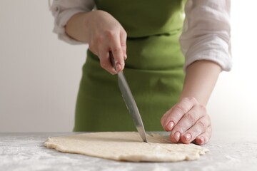 Woman cutting dough at light grey marble table, closeup. Cooking grissini