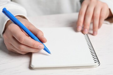 Woman writing in notebook with pen at white wooden table, closeup