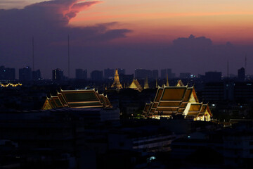 Aerial panoramic view of the Grand Palace complex, backgrounded by the Wat Arun Buddhist temple, during sunset in Bangkok, Thailand.
