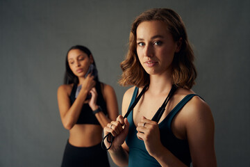 Confident young women in sportswear holding jump rope over shoulder while taking a break - obrazy, fototapety, plakaty