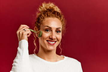 Portrait of a blonde woman, who uses a jade roller to massage her face, for perfect skin.