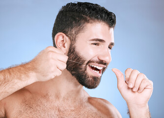 Oral, floss and dental hygiene with a man in studio on a blue background cleaning his teeth for...
