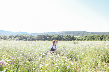Fototapeta na wymiar a woman in a hat sits in a daisy field walk in nature rest traveling