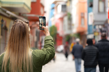 Woman taking photo with phone in the street back view