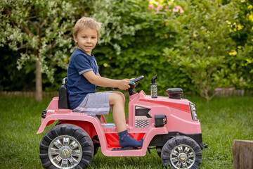 Preschool child, blond boy, riding a tractor in a garden