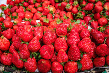 Lots of red, ripe, delicious strawberries lie draped in a heap at a weekly market. Seasonal fruit for sale in the market