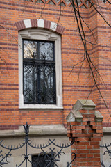 A window in the wall of a house made of multi-colored bricks with a beautiful forged lattice and fence elements.