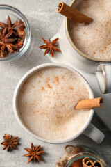 Cups of delicious eggnog with anise and cinnamon on light grey table, flat lay