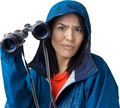 A tourist girl in a blue raincoat holds binoculars in her hands and looks into the distance, spies.