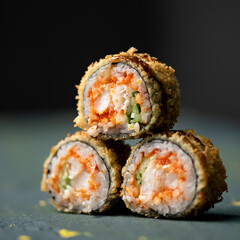 Three sushi rolls in shape of pyramid. Fried sushi rolls with flying fish caviar, shrimp and cucumber. Dark background. Close-up. Side view. Soft focus. Copy space. 