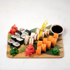 Large set of sushi rolls on wooden plank. Different types of sushi rolls are served with sauce, ginger, wasabi, hiashi. Japanese food. Isolate on white background. View from above. Copy space.