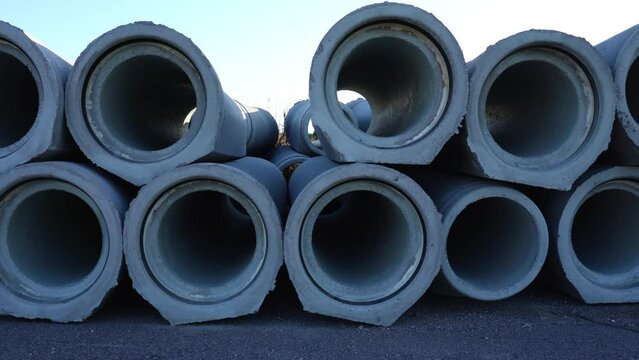 Motion along stacked concrete pipes from cross section ready to install lying on ground at open construction site on sunny day