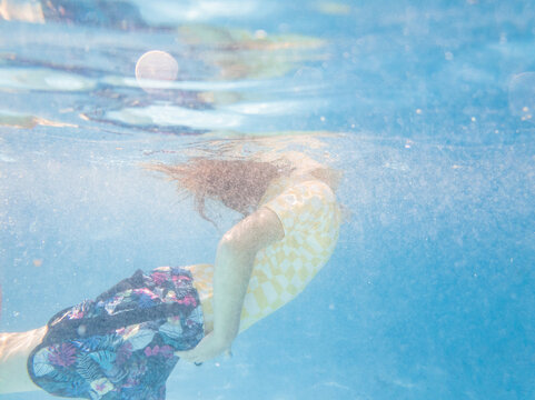 Underwater image of girl coming up to breath air in backyard pool while palying